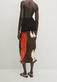 Top corto lavorato a maglia nera con schiena scoperta abbinato a una gonna midi con motivo marrone, arancione e bianco e sandali flat.