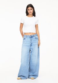 Lichtblauwe wijde jeans met een hoge taille en een klassieke five-pocket ontwerp, gecombineerd met een strakke witte katoenen crop top.