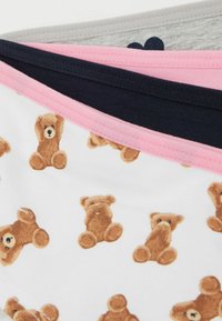 Tres pares de braguitas de algodón; una tiene un fondo blanco con estampados de ositos de peluche marrones, las otras son de colores sólidos: gris, azul marino y rosa, con cinturas a juego.