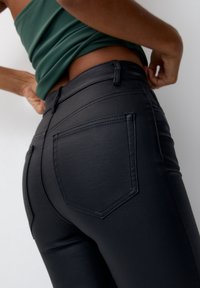 Czarne dżinsy z denimu o dopasowanym kroju, charakteryzujące się gładką teksturą, standardowym przeszyciem oraz dwoma tylnymi kieszeniami. Stylizowane z zielonym topem.