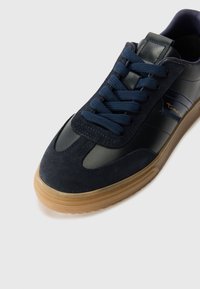 Sneaker blu navy con tomaia in suede e pelle, chiusura con lacci, suola in gomma naturale e brandizzazione discreta sul lato.