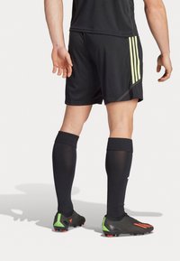 Pantaloni sportivi neri con strisce gialle e calze nere alte fino al ginocchio. Le calzature presentano una parte superiore nera con accenti verdi e rossi.
