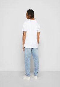 T-shirt bianca a maniche corte con colletto rotondo, abbinata a jeans in denim azzurro chiaro, con vestibilità rilassata e orli risvoltati.