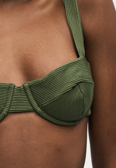 Gros plan d'un haut de bikini côtelé vert olive avec des bretelles épaisses sur une peau foncée.