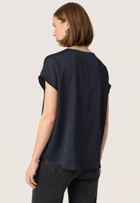 Top de manga corta azul marino con tejido texturizado, corte relajado y dobladillo curvado, combinado con jeans oscuros.
