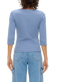 Lichtblauwe geribbelde langwerpige top met een ronde halslijn, gegolfde onderrand en een aansluitende pasvorm, gecombineerd met high-waisted denim cargobroek.