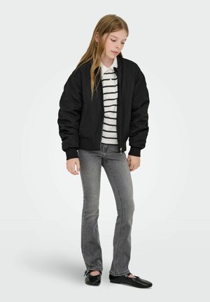 Must bomberjakk valge ja musta triibulise särgi üle, kombineeritud hallide teksade ja mustade kingadega. Komplekti iseloomustab avar lõige ja klassikaline disain.