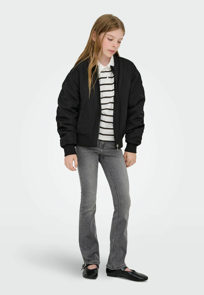 Črno bomber jakno prek bele in črno črtaste majice, kombinirano z sivimi kavbojkami in črnimi čevlji. Obleka ima sproščen kroj in klasičen dizajn.