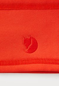 Close-up of red fabric with folded edge and embroidered logo resembling a curled fox head in matching red thread.