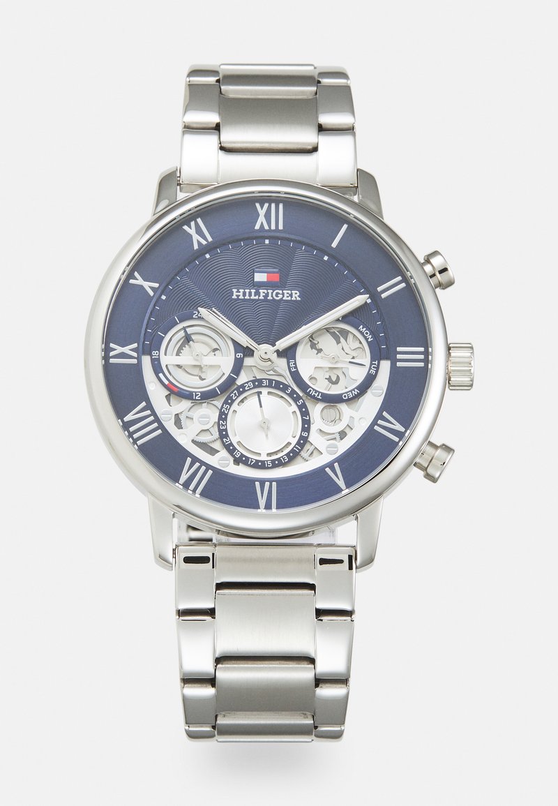 Orologio in metallo argento con quadrante blu testurizzato, caratterizzato da numeri romani, funzioni cronografiche e un cinturino a tre maglie.