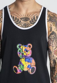 Čierny tielko s farebnou grafikou žuvacej medvedíkovej cukrovinky. Obsahuje kontrastný biely lem. Materiál vyzerá ľahký a hladký.