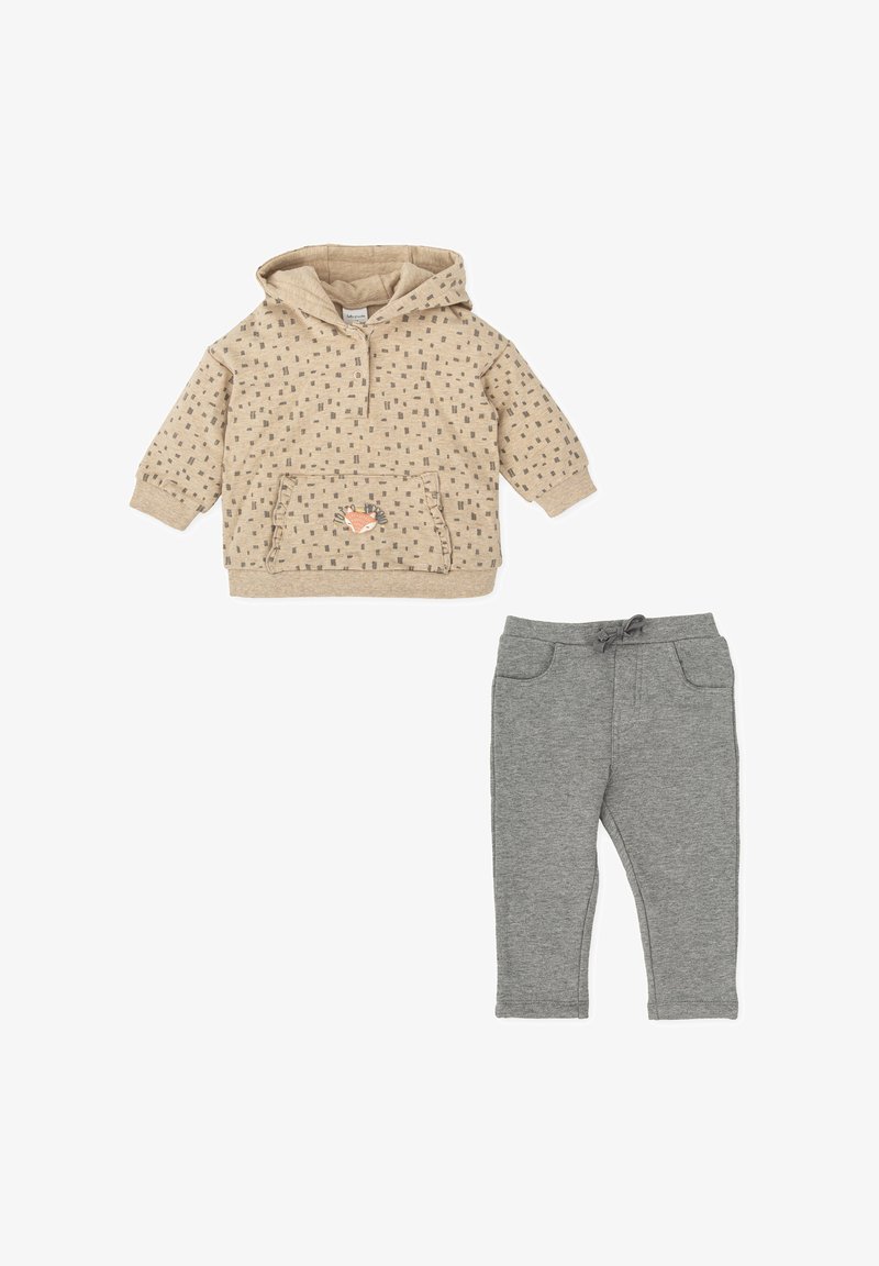 Sudadera beige con capucha y un patrón texturizado, bolsillo frontal y un aplique de zorro, combinada con pantalones grises elásticos con bolsillos falsos.