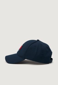 Marineblå baseball cap med en lett buet skjerm, stoffmateriale og sidelogo med røde og hvite detaljer. Justerbar stropp bak.