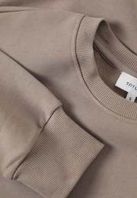 Felpa color marrone chiaro con collo e polsini a costine, realizzata in un tessuto morbido con una texture liscia; l'etichetta indica la taglia 'S'.