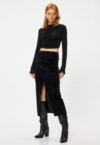 Zwarte lange mouwen crop top van textuurstof met ruching aan de voorkant, gecombineerd met een bijpassende hoge taille rok met een voorkeursplit en een zachte textuur.
