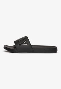 Sandal in pelle nera con una larga fascia che presenta un logo in rilievo, materiale in gomma liscia, soletta sagomata e design minimalista.
