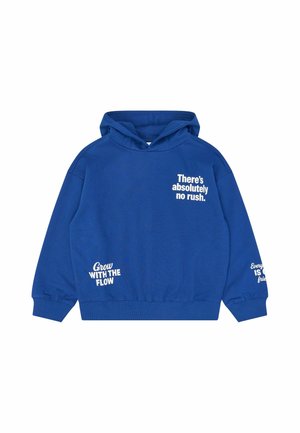 Sudadera azul con capucha y tres textos en blanco: "No hay absolutamente prisa", "Crece con el flujo" y texto parcialmente visible en la manga.