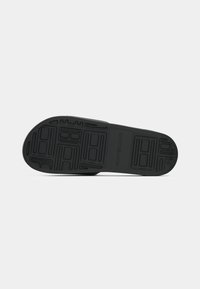 Black shoe sole with rectangular and linear tread patterns, including the embossed "Tommy Hilfiger" logo in the center.