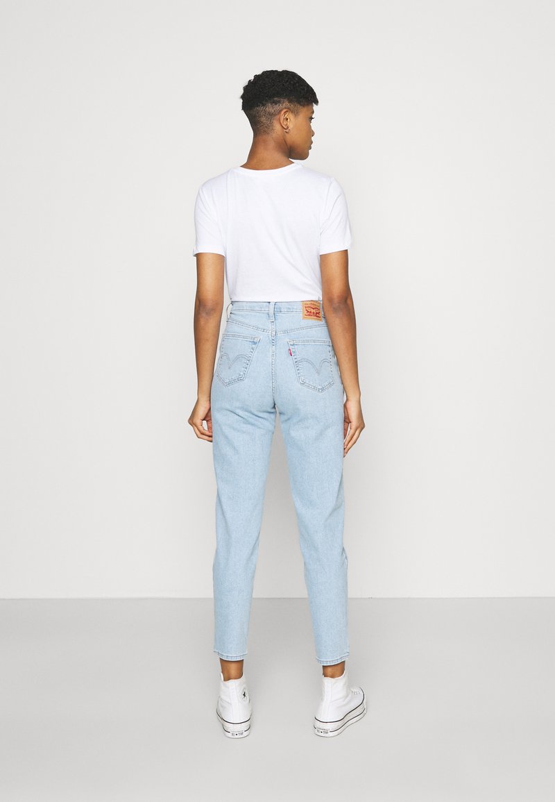 Hellblaue hoch geschnittene Jeans mit schmalem Bein, ausgestattet mit Gesäßtaschen mit geschwungenen Nähten, kombiniert mit einem schlichten weißen T-Shirt und weißen Sneakern.