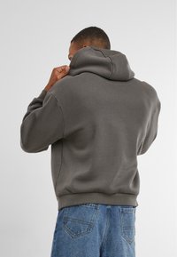 Sudadera de algodón gris con una costura central en la parte posterior, gran capucha y puños y dobladillo acanalados, combinada con jeans de mezclilla azul.