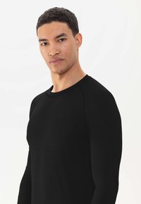 Chemise noire à manches longues avec un col rond et des manches raglan. Fabriquée dans un tissu lisse, sans motifs ni accents visibles.