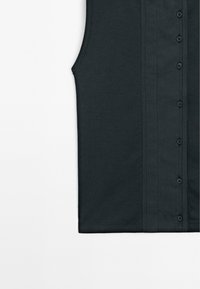 Ærmeløs sort ribbet top med knaplukning foran, synlige syninger langs knappanelet og rund ærmegab.