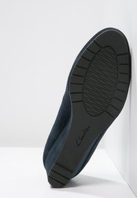 Scarpa in suede blu con design arrotondato e suola in gomma nera texturizzata con motivo a rilievo; logo Clarks impresso sulla suola.