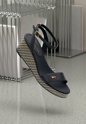 Navy wedge sandal with a woven striped platform, ankle strap, and gold hardware accents. Smooth texture with a flat toe design.