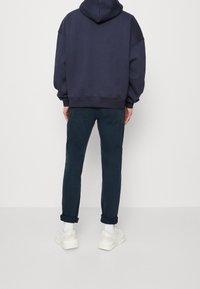 Sudadera azul marino de gran tamaño con capucha ajustable, combinada con pantalones azul marino oscuros arremangados en los puños y zapatillas ligeras.