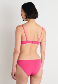 Rosa bikini sett med myk stoff, justerbare stropper og krokfeste. Bunnen har en moderat utskjæring og glatt tekstur.