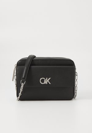 Black faux leather crossbody bag with a zip closure, silver chain strap, and CK logo on the front. Simple rectangular design.