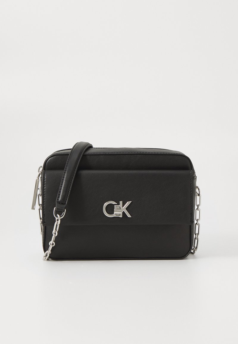 Melnas mākslīgās ādas crossbody soma ar rāvējslēdzēju, sudraba ķēdes siksnu un CK logo priekšpusē. Vienkārša taisnstūra forma.