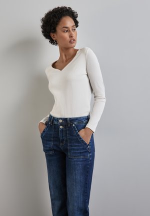 Haut blanc à manches longues avec un col en V associé à un jean en denim bleu à taille haute, avec de grandes poches avant et une fermeture à deux boutons.