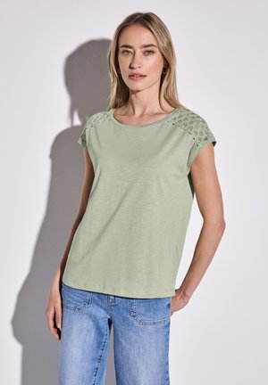 Light green cotton T-shirt with short sleeves, featuring lace detail on shoulders, relaxed fit, and a round neckline, paired with blue jeans.