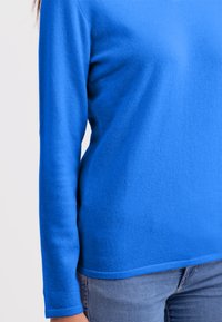 Maglione blu a maniche lunghe realizzato in un tessuto a maglia liscia, con scollo rotondo e silhouette aderente. La parte inferiore ha un orlo dritto.