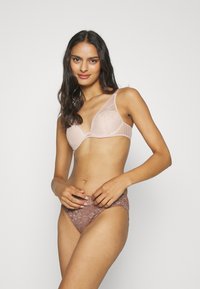 Spitze-BH in sanftem Rosa mit geformten Körbchen und breiten Trägern, kombiniert mit passendem braunen Spitzen-Slips mit floralem Muster und gewelltem Saum.