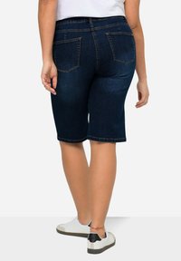 Pantalones cortos de denim azul oscuro con un corte recto, de longitud a medio muslo y bolsillos traseros estándar. Costuras visibles y una textura suave.