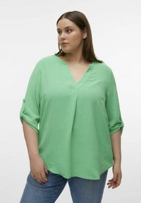 Blouse vert clair, texturé, avec un décolleté en V et des manches trois-quarts. Le tissu est doux et le design présente une coupe ample.