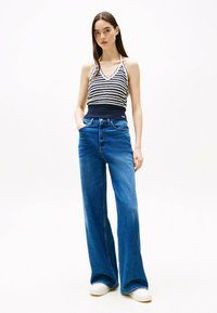 Top de halter a rayas en azul marino y blanco con bordes en forma de ondas, combinado con jeans de tiro alto y pierna ancha en azul y zapatillas blancas.