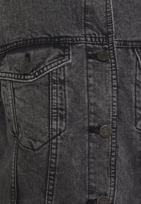 Giubbotto in denim nero con due tasche frontali, bottoni a pressione argentati e una finitura testurizzata con dettagli di cucitura visibili.