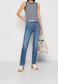 Blå denimjeans med rak passform, kombinerat med en marinblå och vit randig linne. Beige klacksandaler med blockklack och en mönstrad handväska.