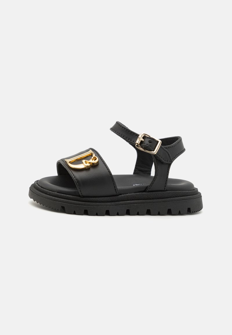 Sandales ouvertes en cuir noir avec une sangle de cheville réglable, détail en boucle dorée et semelle en caoutchouc noir épaisse avec un motif de crampons.