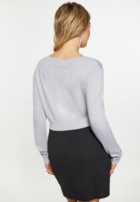 Szürke, cropped pulóver hosszú ujjal, puha tapintású, széles nyakkivágással; egy testhez simuló fekete szoknyával párosítva. Egyszerű dizájn, amely elegáns megjelenést kölcsönöz.
