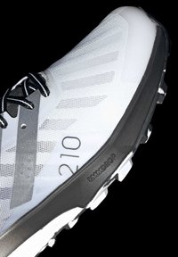 Zapatilla deportiva blanca con parte superior de malla, acentos negros y suela gruesa negra. Presenta la talla visible "210" y la marca "8MMDROP".