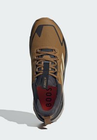 Brązowe i czarne buty trekkingowe z teksturowaną siateczką górną, wyraźnym systemem sznurowania oraz czerwoną wkładką wewnętrzną z napisem "BOOST".