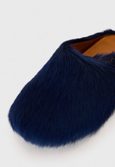 Chaussure de salon en fourrure marine à bout arrondi et texture douce, avec un intérieur lisse de couleur beige.