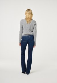 Grijze gebreide trui met lange mouwen, gecombineerd met donkerblauwe flared jeans. Opvallende details zijn de stiksels op de zakken en de gestructureerde afwerking.