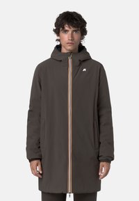 Cappotto esterno marrone con cappuccio, chiusura frontale con zip caratterizzata da strisce colorate e tasche laterali, realizzato in materiale liscio e resistente all'acqua.