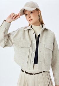 Hellgraue Wolle-Mischung kurze Jacke mit Druckknöpfen, zwei Fronttaschen und einem spitzen Kragen, kombiniert mit einer passenden Mütze und einem cremefarbenen Oberteil.