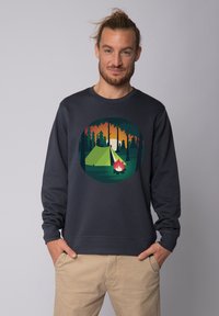 Donkerblauwe sweatshirt met een cirkelvormige graphic van een camping met een tent en kampvuur, tegen een achtergrond van zonsondergang en bos.